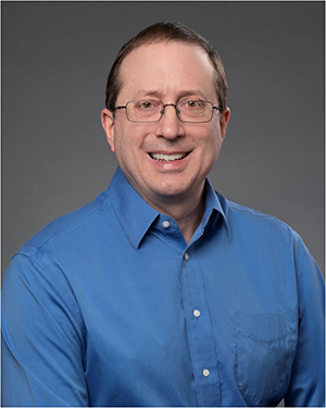 A head shot of Dave Gretta, who is a white man with brown hair, glasses, and a blue collared shirt